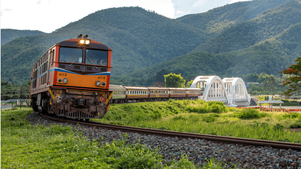 Train in Northern Thailand between Chiang Mai and Bangkok, in the countryside, with mountains in the backdrop.